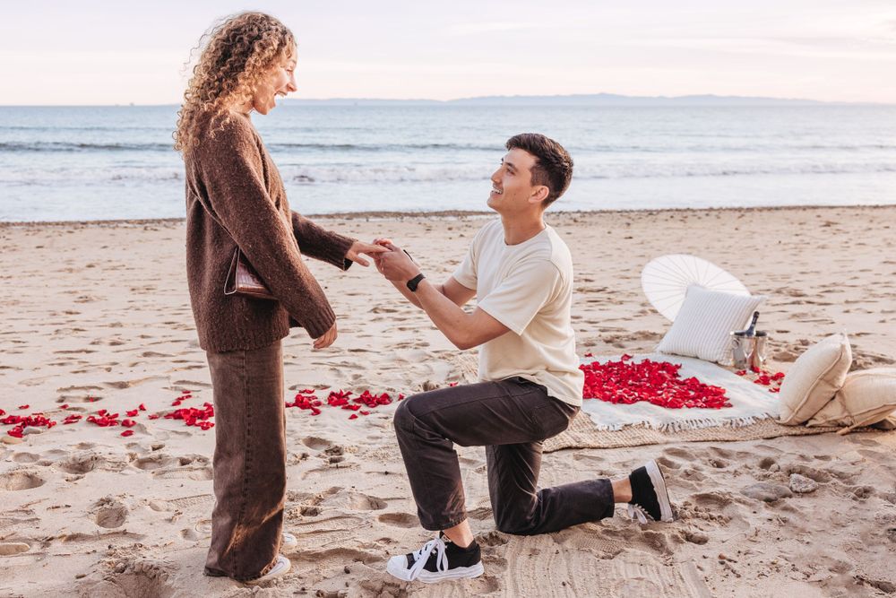 A surprise beach proposal with red rose petals scattered along the shoreline.