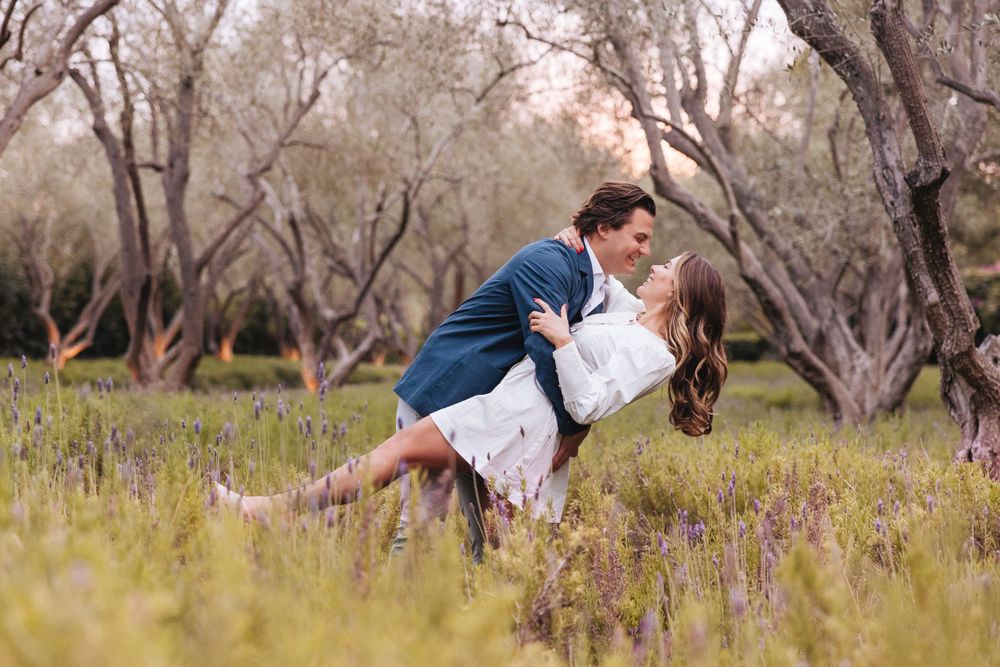 A romantic scene in a meadow with wildflowers and trees where a couple shares an intimate dance-like embrace.