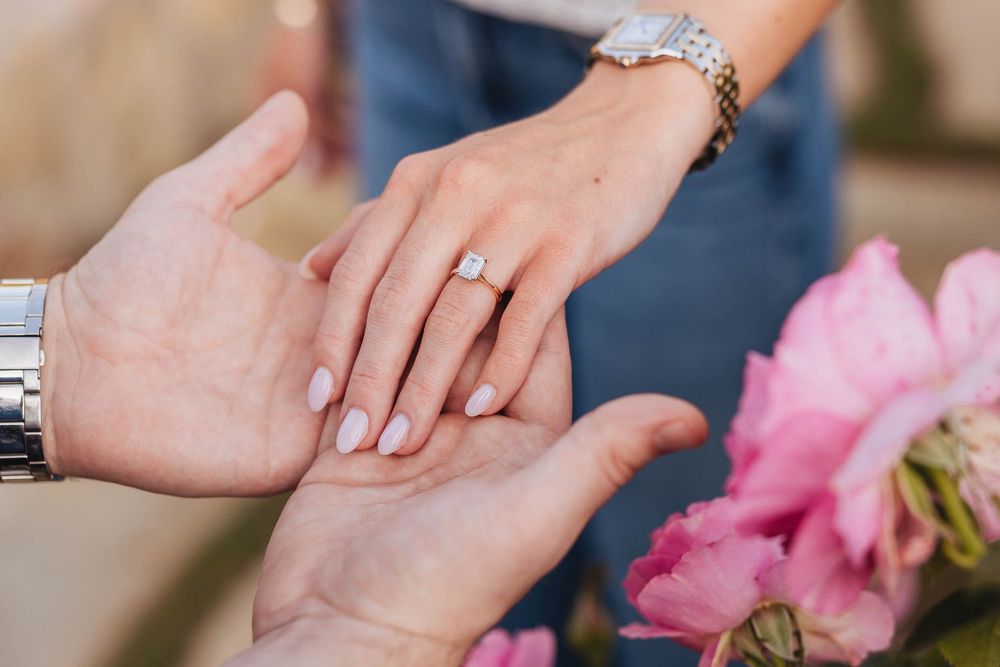 A close-up series of hands exchanging wedding rings during a ceremony with pink flowers in the background.