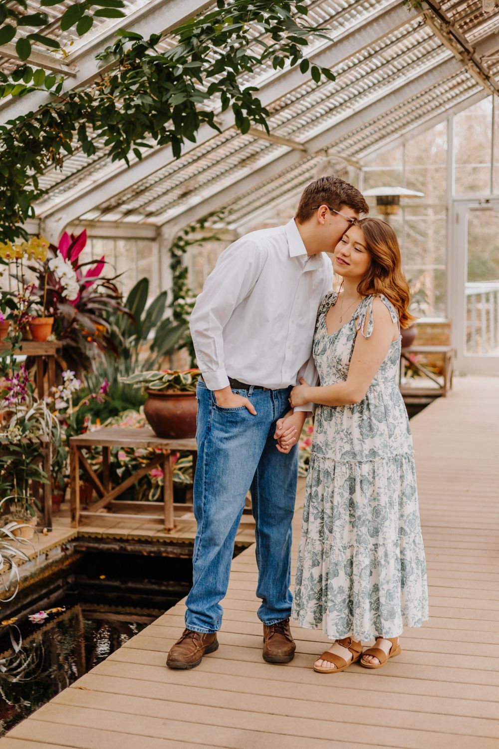 Couple shares tender moments in a sunlit greenhouse filled with tropical plants.