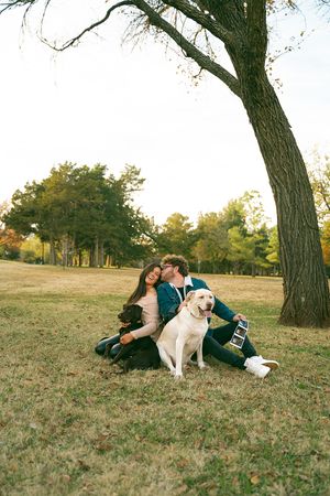 A couple relaxes on grassy hill with their dogs during sunset.