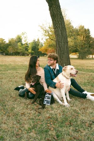 A couple and their dog laying in autumn grass while holding ultrasound photos.