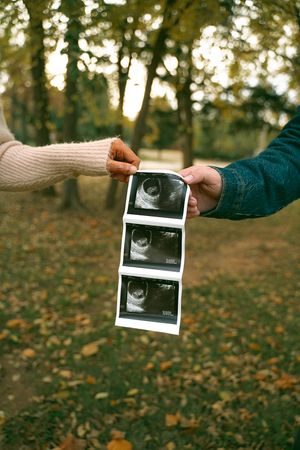 Hands passing ultrasound photos in a fall outdoor setting with bokeh lighting.