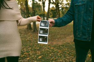 Hands exchanging ultrasound photos against a backdrop of autumn trees.