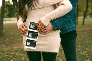 Couple sharing a tender moment while holding ultrasound photos in autumn setting.