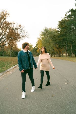 Couple walking together on an autumn path with fallen leaves and trees in the background.