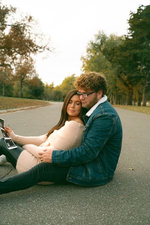 Couple relaxing on pavement while looking at a device together in fall setting.