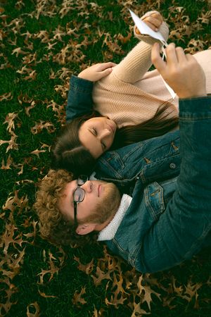 Two people laying on fallen autumn leaves while sharing a tender moment.