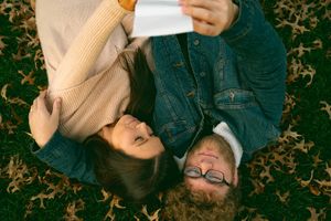 Couple viewing something on mobile devices while relaxing on ground covered in fall leaves.