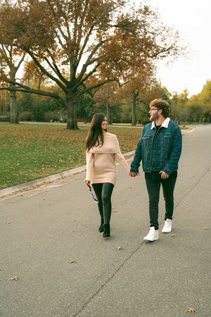 Couple walking casually on paved path surrounded by autumn trees.