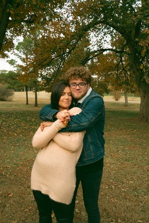 A tender moment shared between two people in a park with fall foliage in the background.