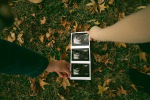Autumn leaves scattered on the ground with someone holding ultrasound photos.