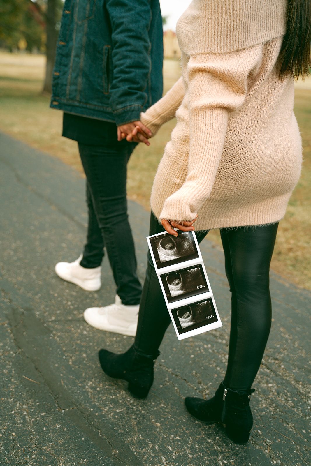 Close-up of feet and legs walking while holding ultrasound photos on an autumn day.