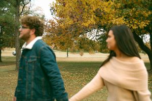A couple shares a joyful moment together in a park with autumn trees.