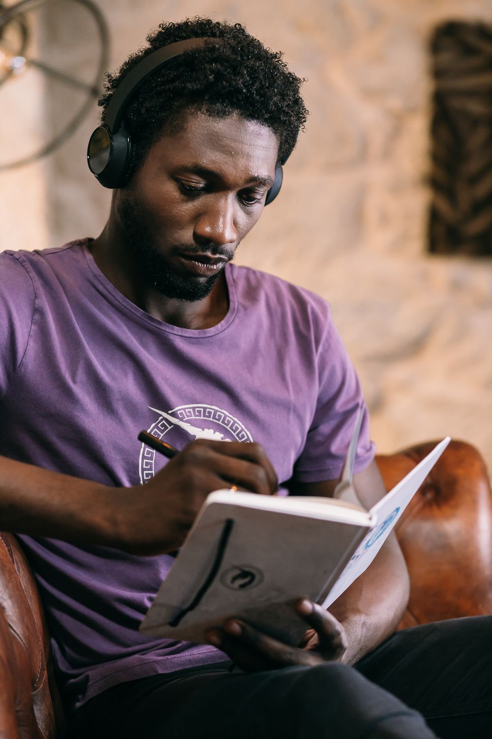 Person wearing a purple t-shirt sits comfortably on a leather couch while reading from a digital tablet.
