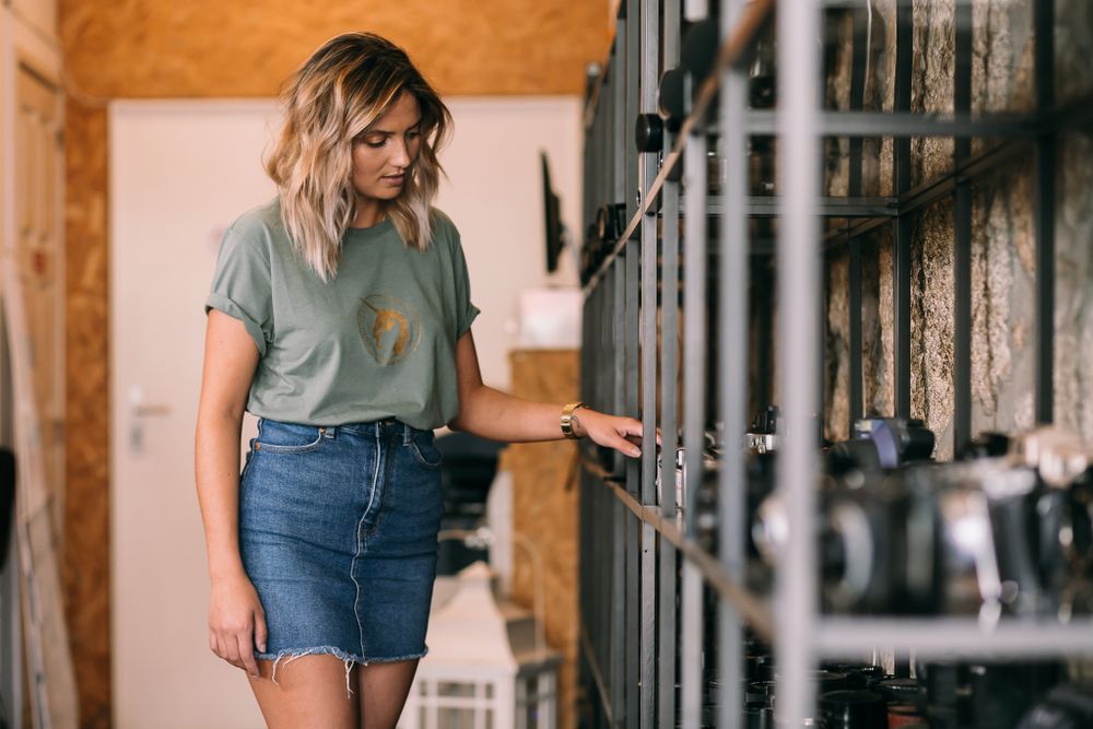 A person in a casual gray t-shirt and denim skirt stands near gym equipment in a fitness facility.