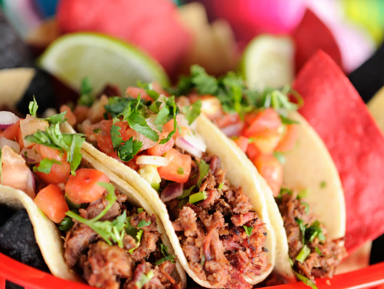 Fresh street tacos garnished with cilantro and lime served in a red basket.