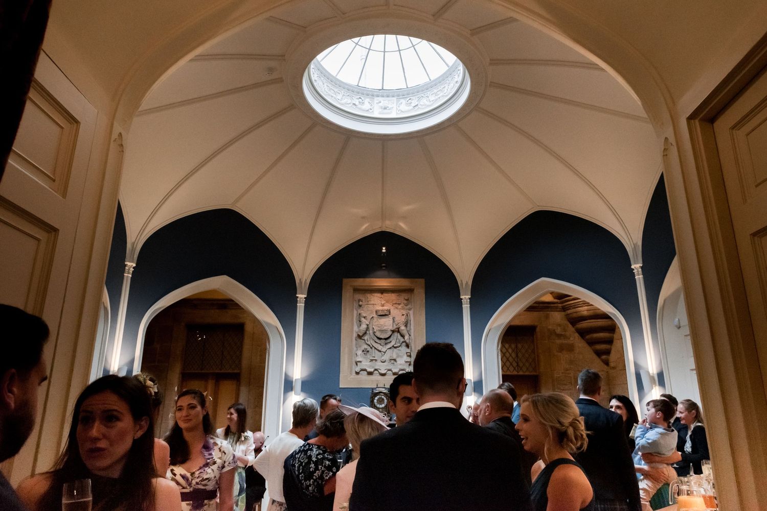 Elegant domed architectural interior with a skylight and arched alcoves filled with guests during a formal gathering.