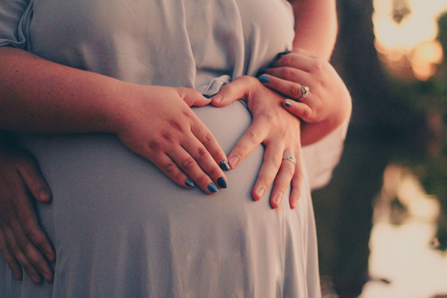 Close-up of hands resting on pregnant belly in soft evening light.