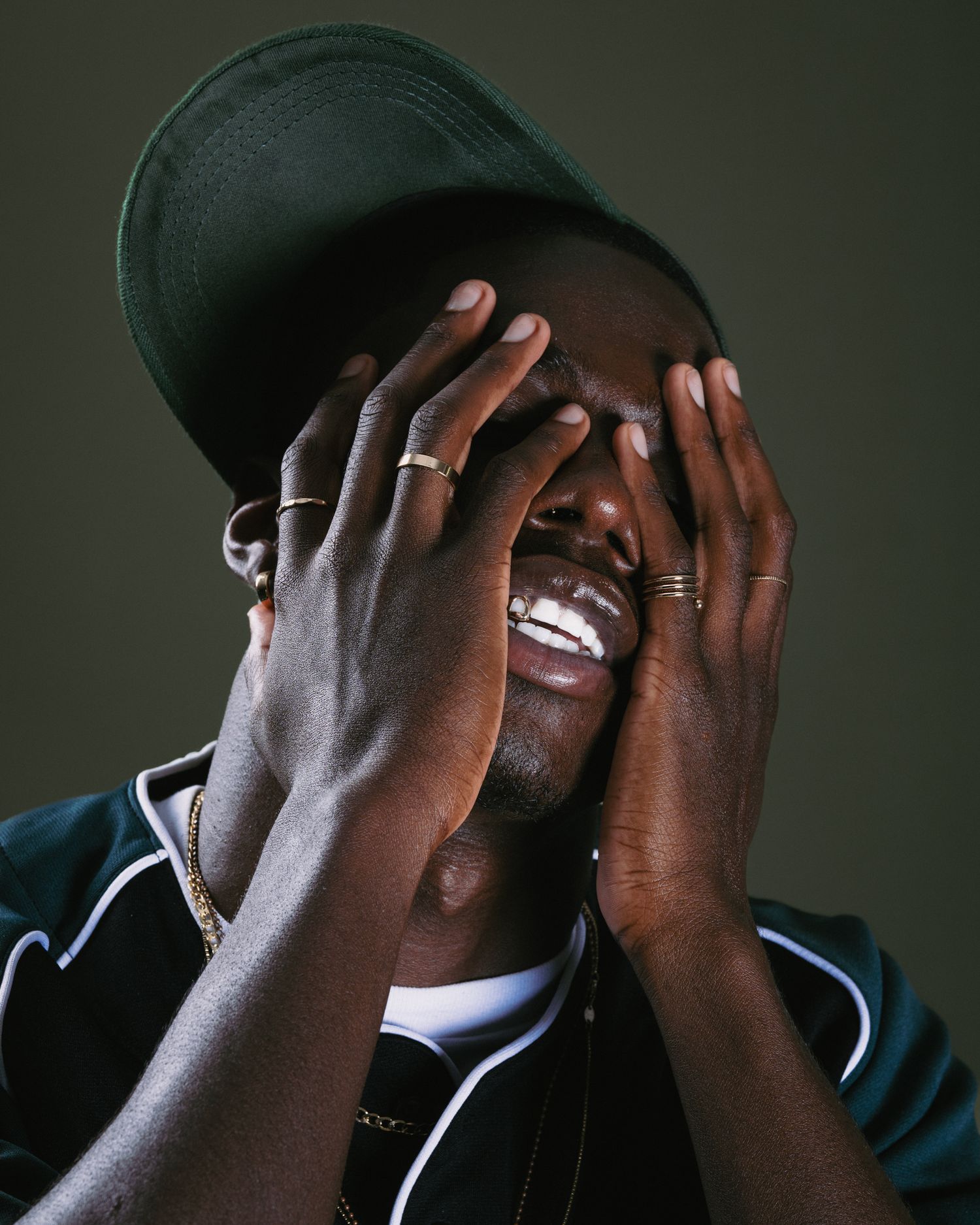 Joyful portrait showing hands covering face with bright smile wearing baseball cap.