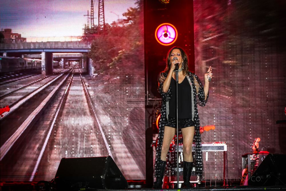 Concert performance with dramatic train track visuals displayed on large screen behind stage.