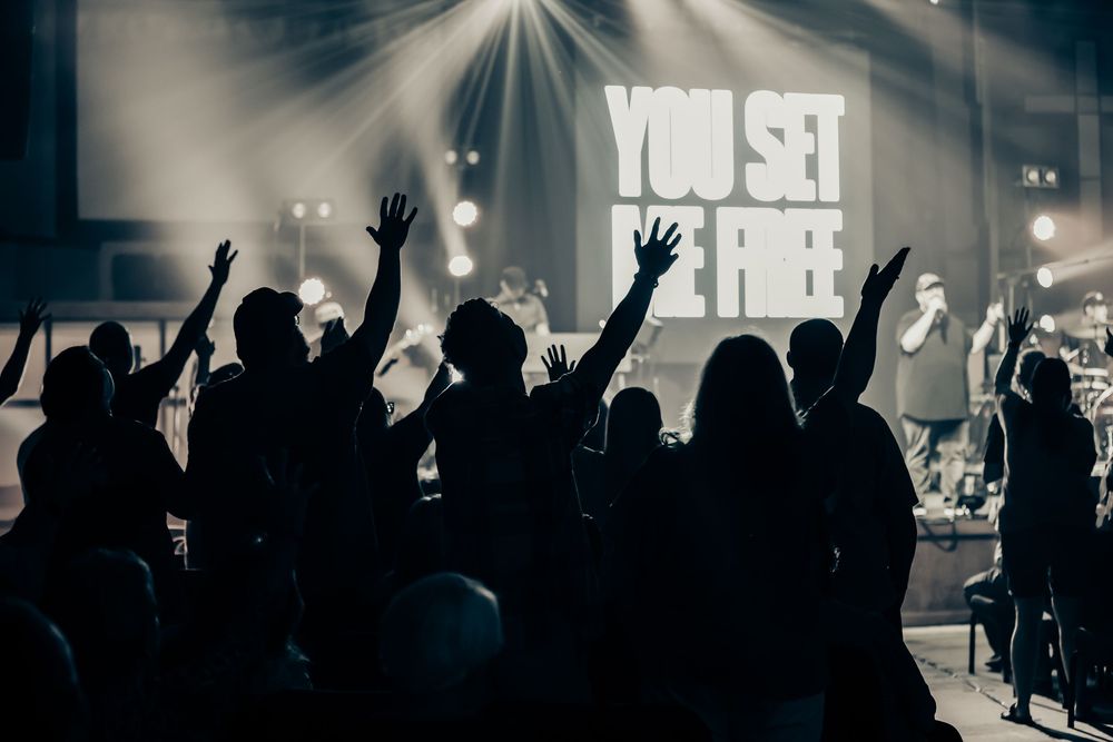 Silhouettes of concert audience with raised hands against dramatic stage lighting.