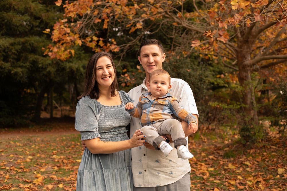 Family photo session in a park setting with warm autumn colors and falling leaves.