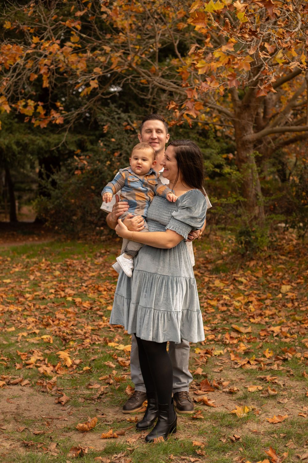 Playful family photoshoot on an autumn day with orange and yellow leaves scattered on the ground.