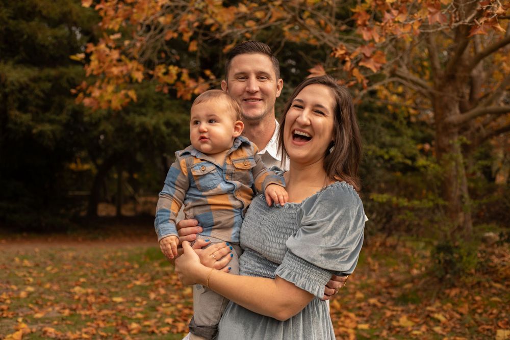 A loving family portrait session captured in a park with beautiful autumn foliage in the background.