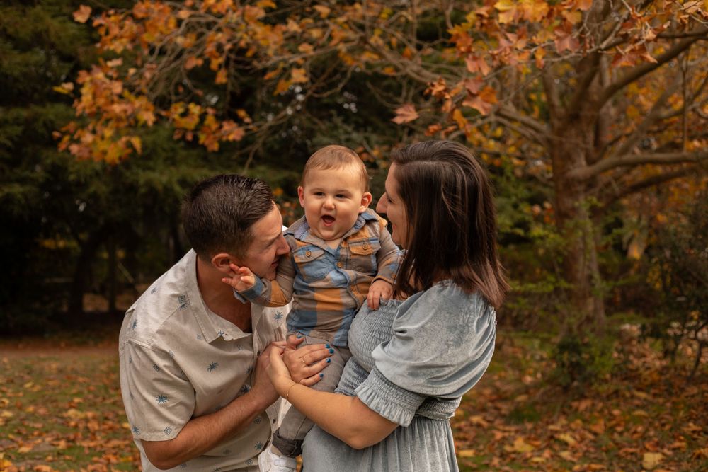 Candid family moment outdoors surrounded by vibrant fall colors and fallen leaves.