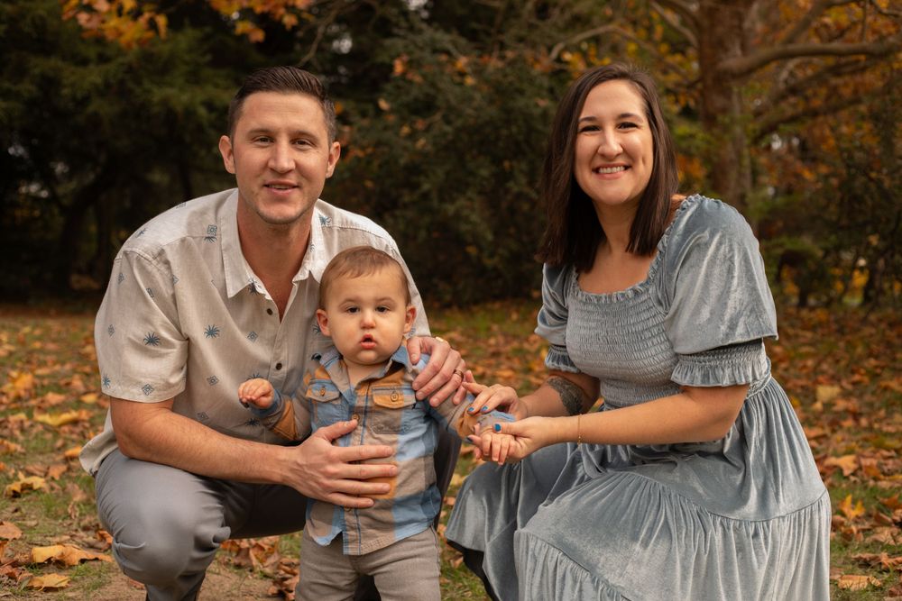 Family posing together against a backdrop of autumn trees with orange and yellow foliage.