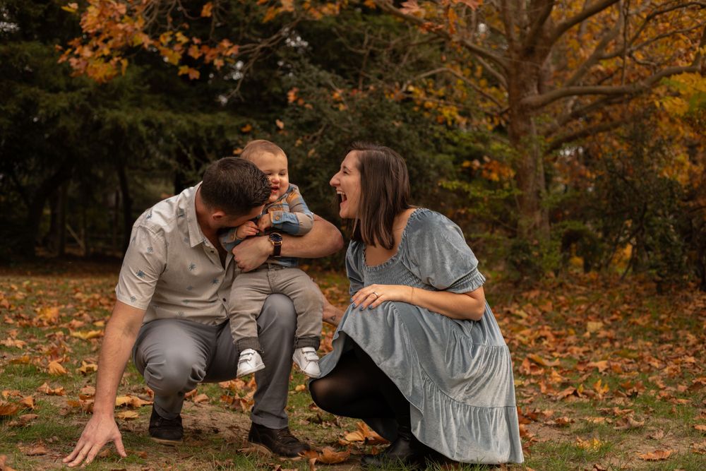 Family shares playful moment together while sitting in a park with fall foliage.