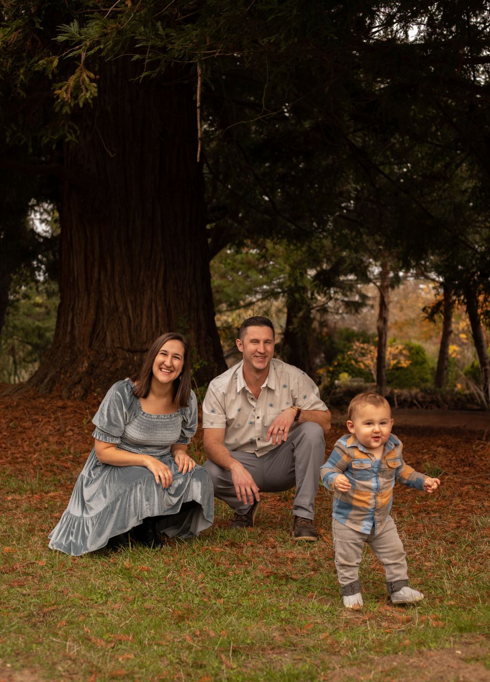 Family outdoor portrait with large tree trunk and autumn foliage in background.