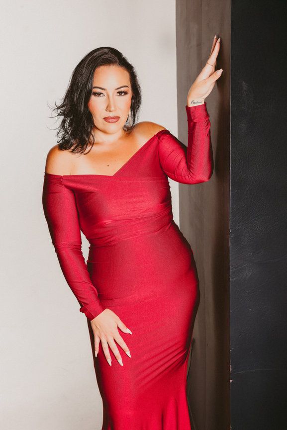 Glamorous pose in a form-fitting red long sleeve dress against a minimalist backdrop.