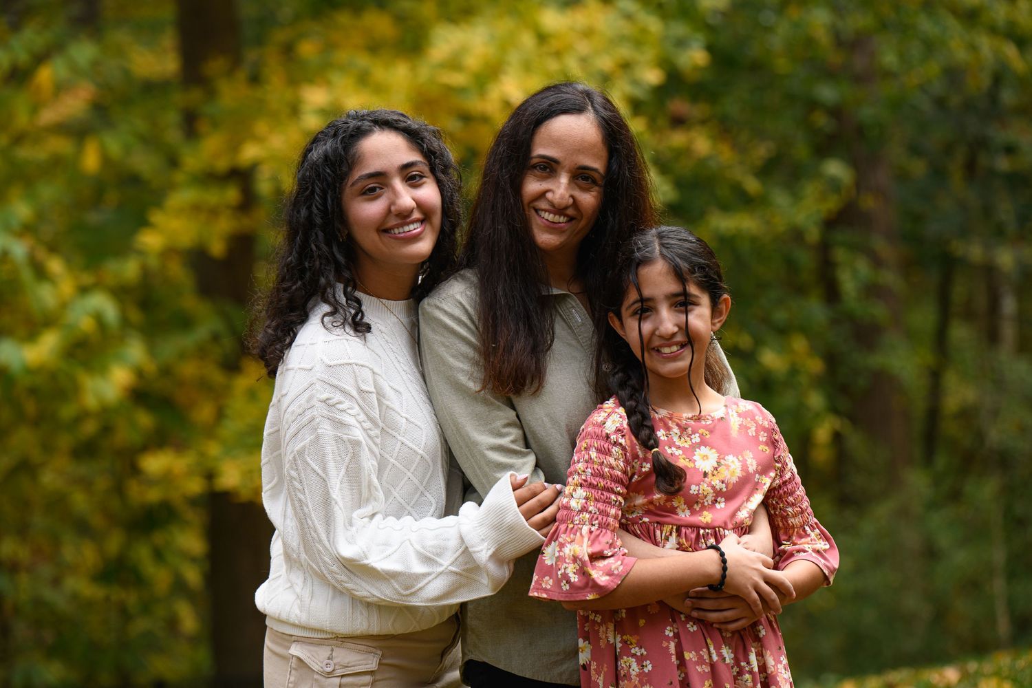 Outdoor autumn family portrait session featuring people embracing and smiling in a wooded setting with warm fall colors.