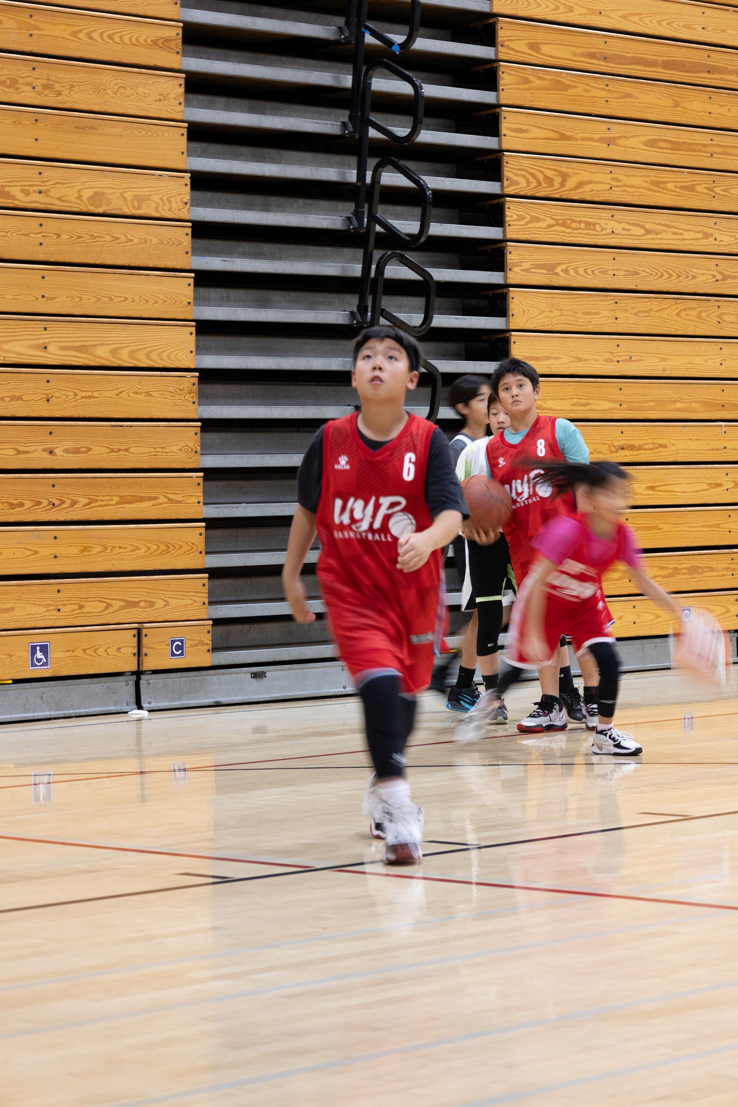 A youth basketball player runs down the court dribbling the ball towards the basket. Candid photograph of determination.