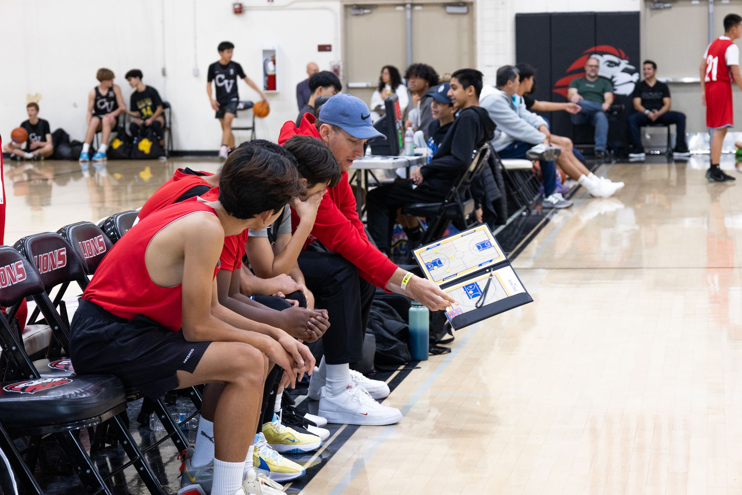 Coach of a youth basketball team share game plans with team on bench. Teammates leaning in to listen to what the coach is saying.