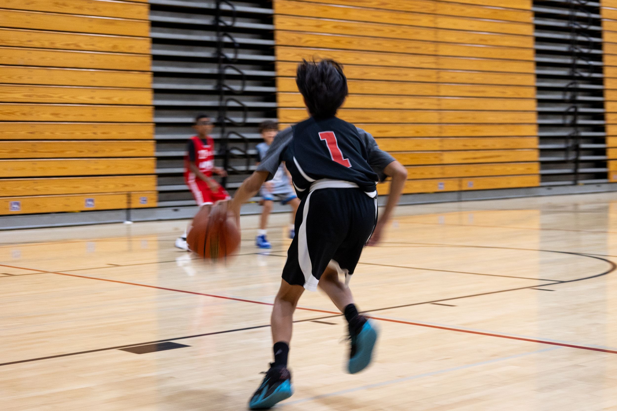 A youth basketball player dribbles his ball out to his team during a game. Action photography capturing motion, speed and team work