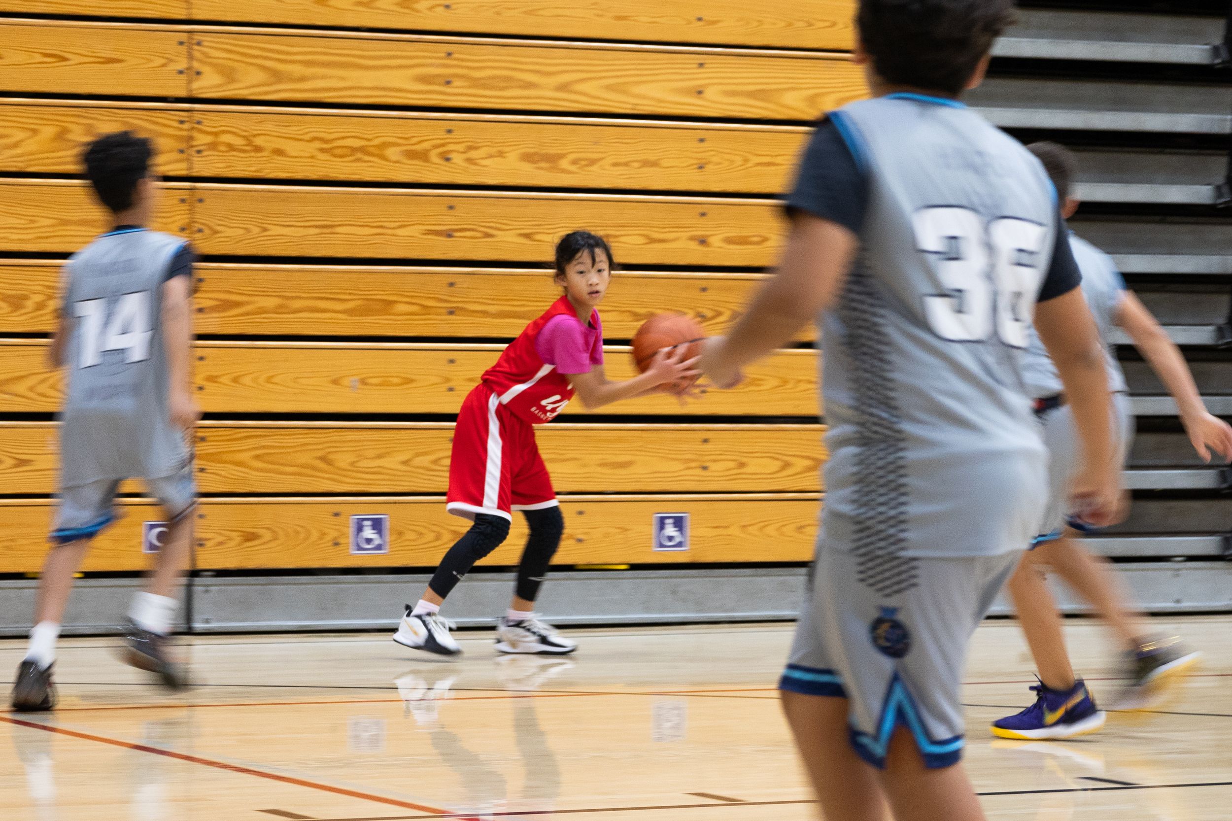 Action sports photography of a youth basketball team. A female player looking to pass the basketball to her team mates on a crowded court.