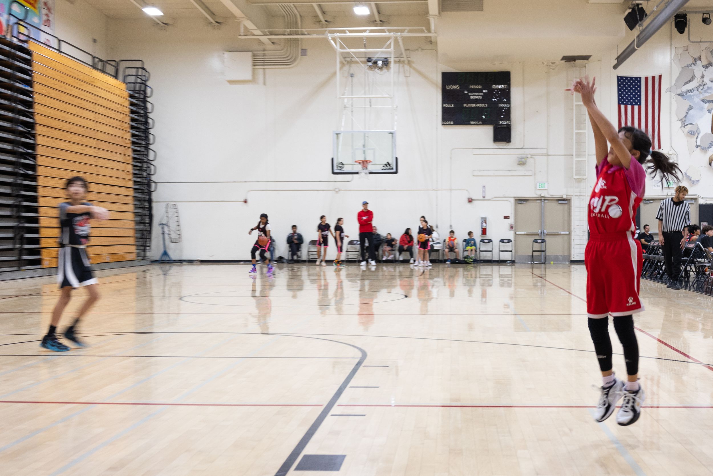 A female youth basketball player shooting a basketball into a basket. She is taking a jump shot. The photo is mid jump of a jump shot.