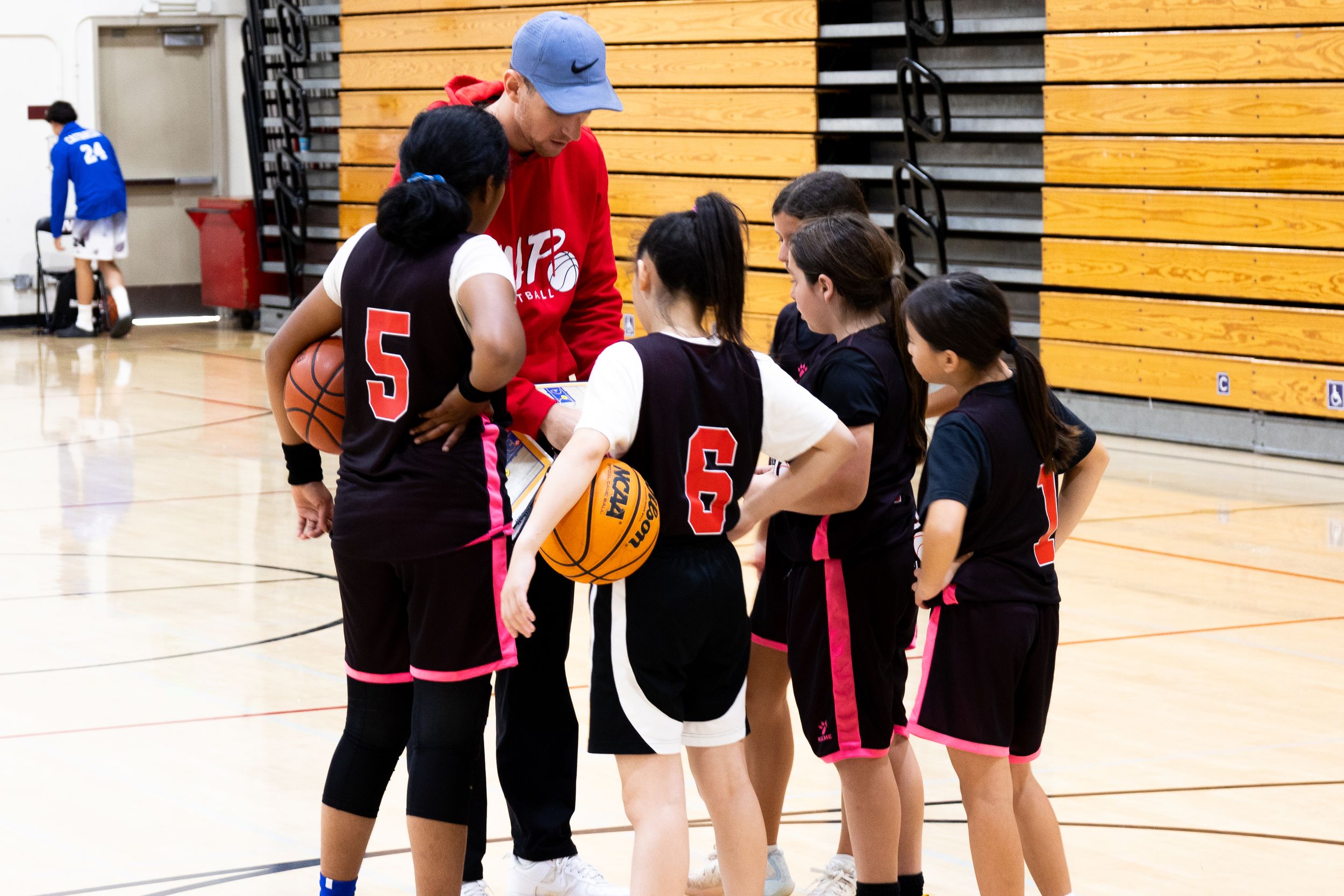 Candid photography of a basketball coach leading a team huddle during a time out showing game plans on a clip board and listening to players