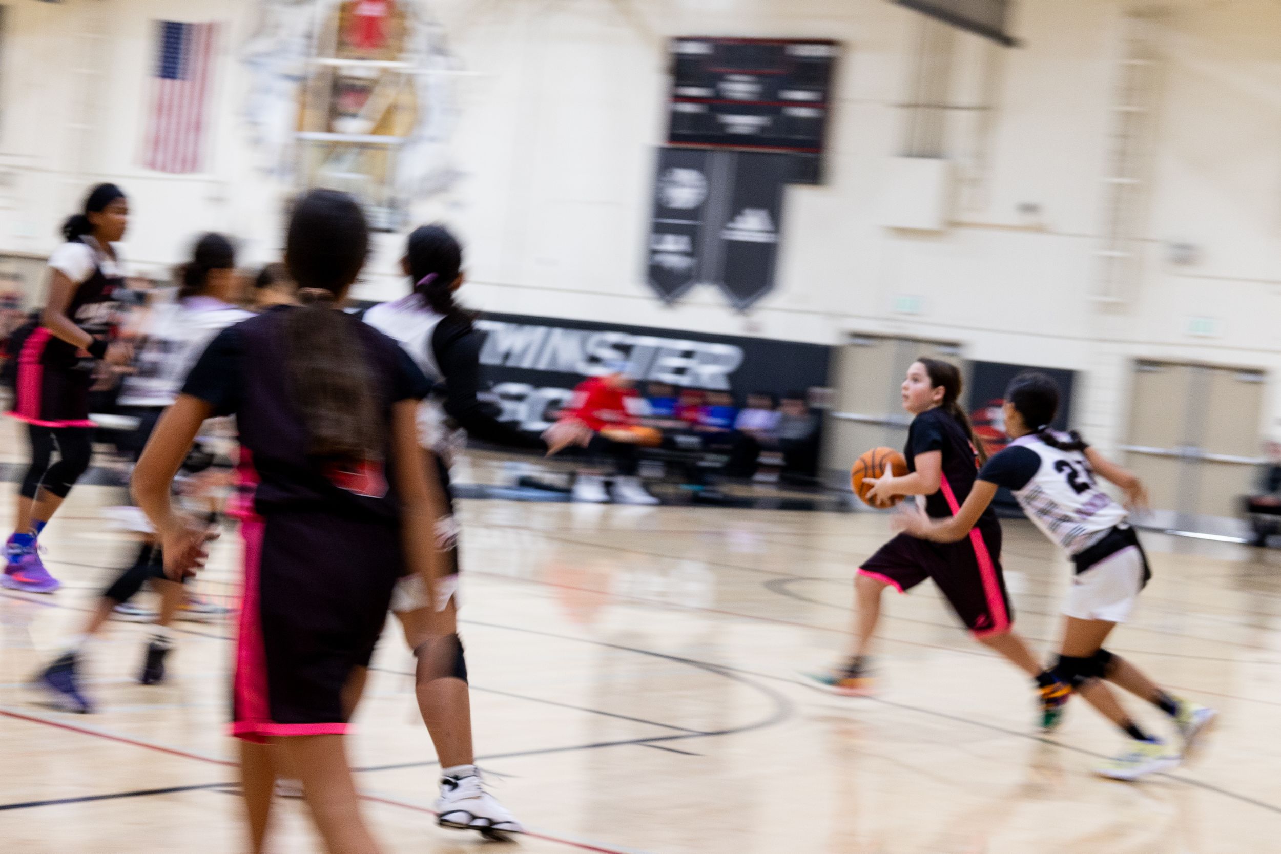 An action photograph of a female basketball player running and dribbling a ball while the background is blurry