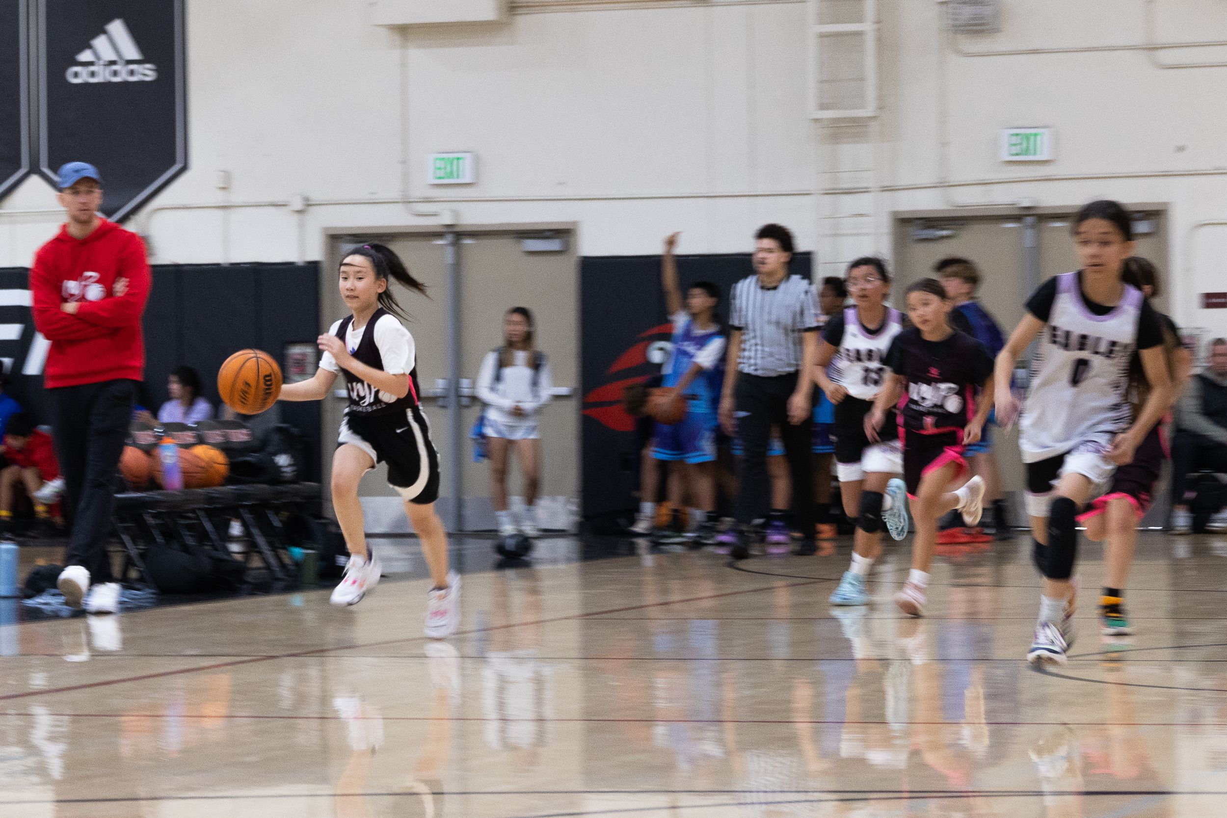 Female youth basketball player dribbling a ball down the court. Playing inside court with blurred background and in focus player