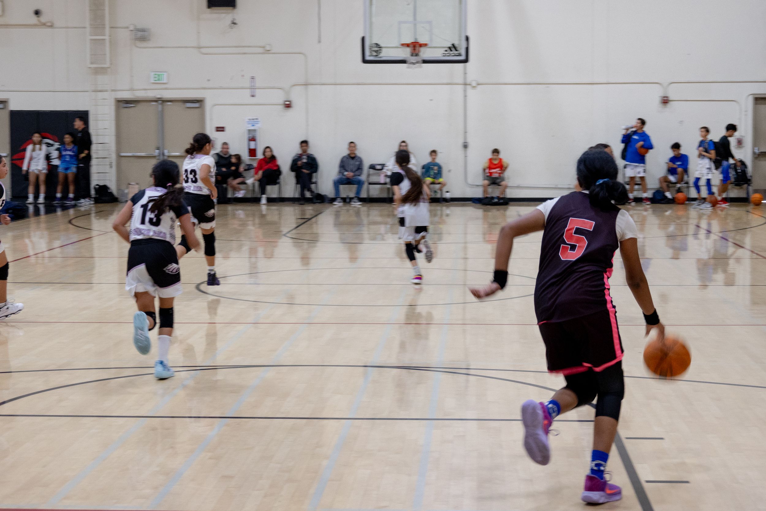 A basketball player dribbles a ball down court to the while the defending players run to the other side of the court