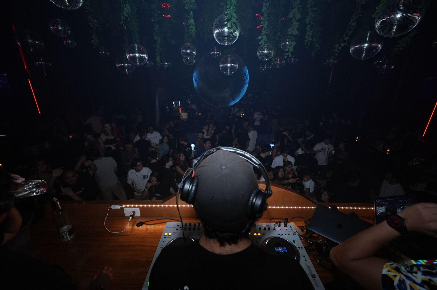 DJ performing at a nightclub with illuminated chandeliers hanging from the ceiling in a dark atmosphere.