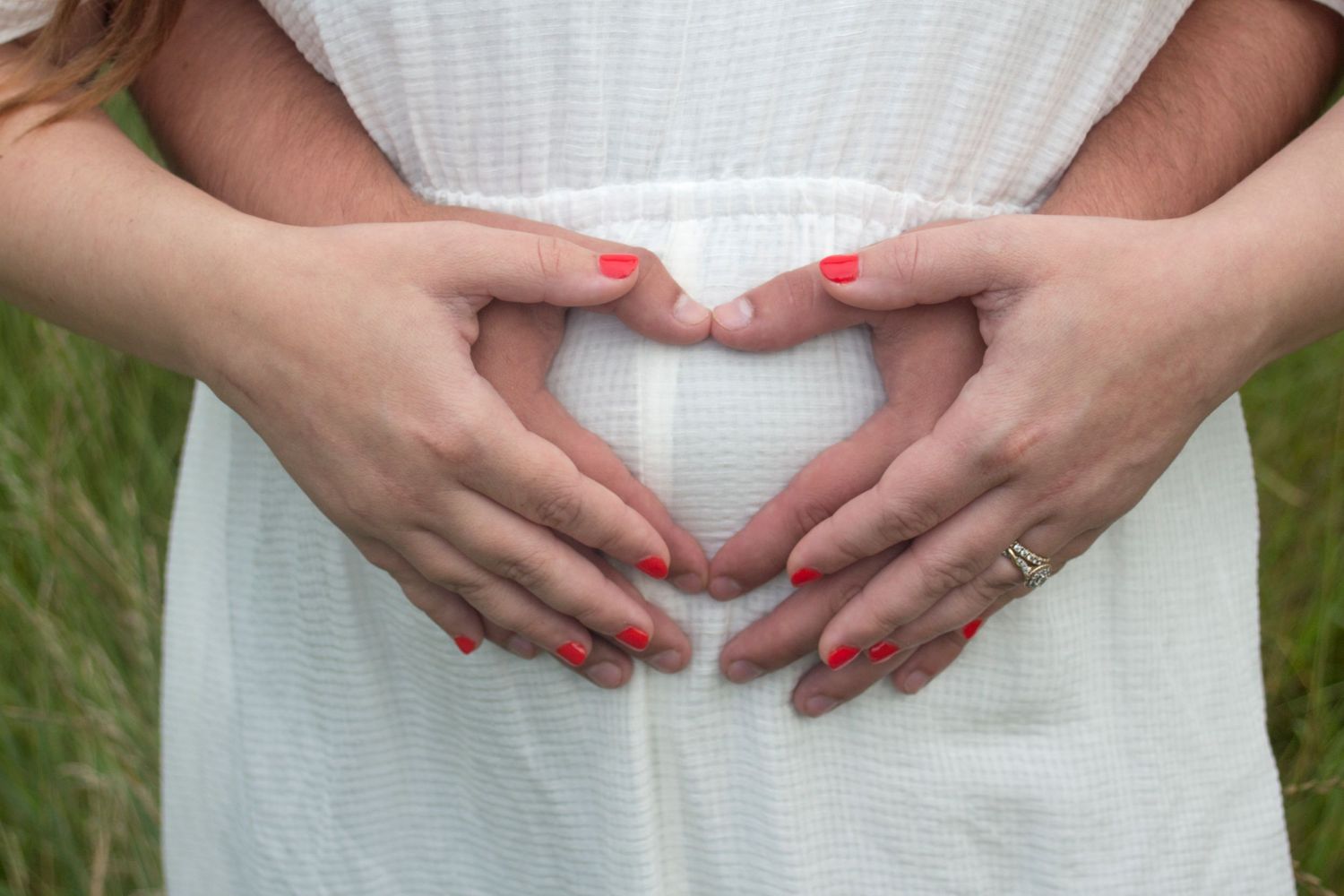 Man and woman's hands forming a heart together over a baby bump.