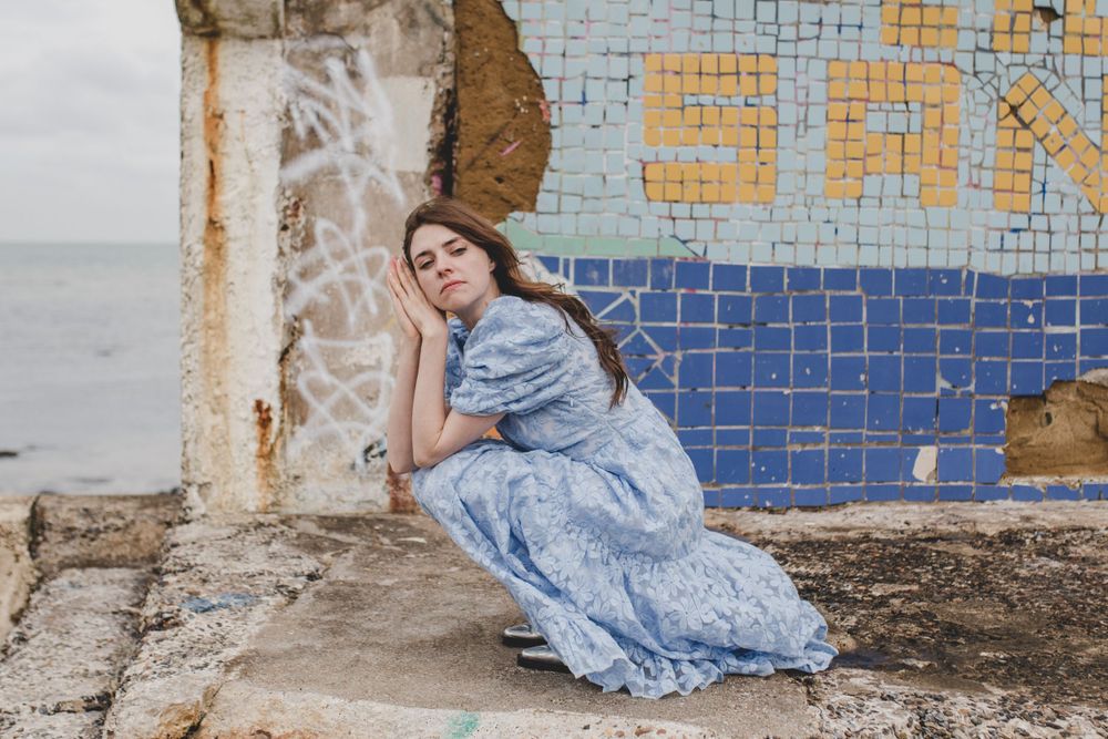 Model in blue dress reclining against mosaic wall by the sea.