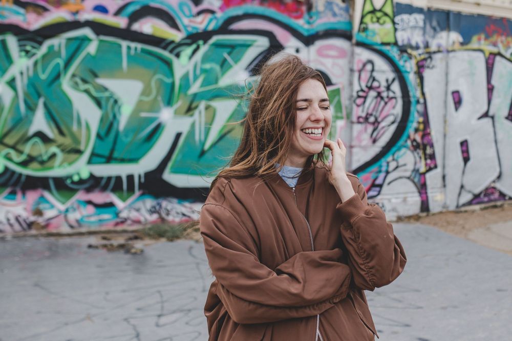 Casual pose in brown jacket against colorful graffiti wall.