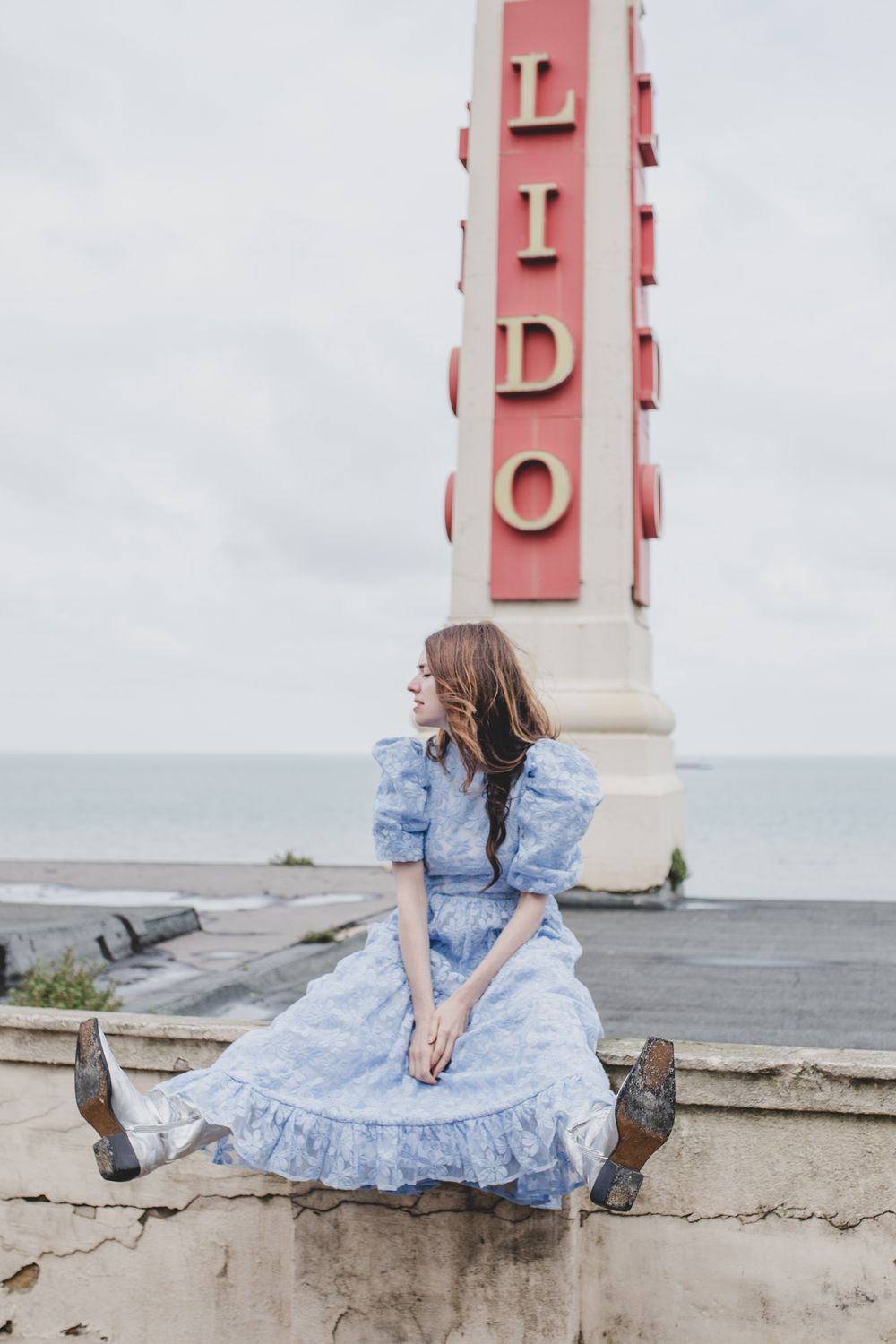 Vintage-style photo of blue dress against pink Lido sign by ocean.