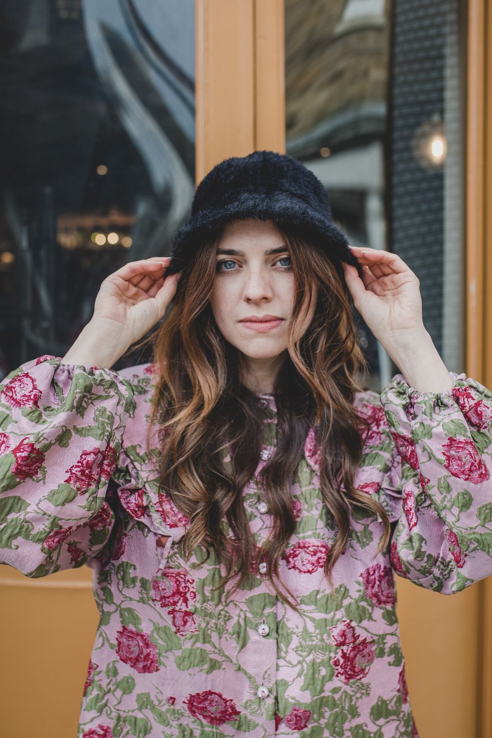 Winter style with furry hat and floral dress outside shop window.